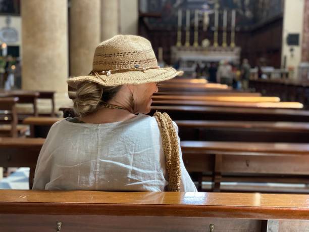 Rear view of grandmother visiting church with her granddaughter, they sitting on bench and praying together