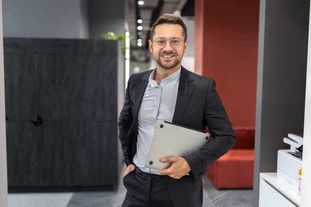 istock Successful businessman wearing suit holding laptop computer in office hall 2154180755