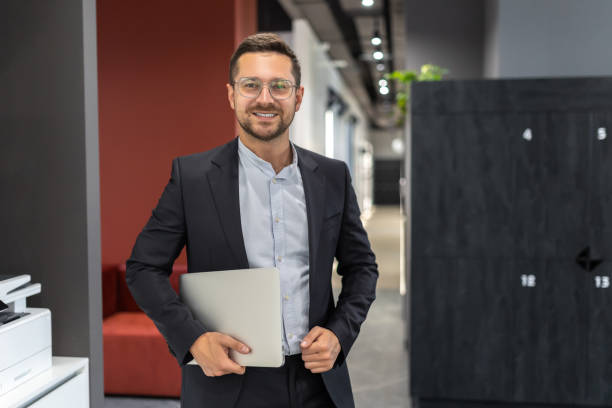istock Successful businessman wearing suit holding laptop computer in office hall 2154180767
