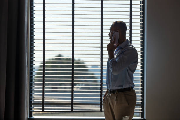 istock Businessman talking confidently on his mobile phone while standing near large windows in office 2154180853