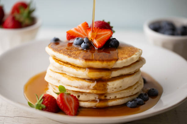 istock pouring syrup on piled pancake with strawberries and bluberries 2154182519