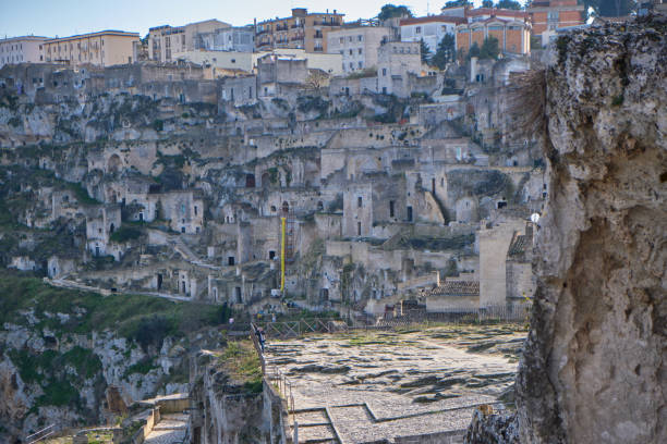 Against the backdrop of Matera's iconic Sassi, or cave dwellings, the silhouette of ancient rooftops creates a striking tableau against the backdrop of the setting sun. As shadows lengthen and golden light bathes the scene, the timeless beauty of this UNESCO World Heritage site is illuminated in all its glory.