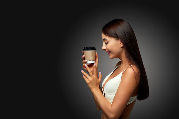 Young brunette woman isolated on a dark background with a gradient wall studio enjoys holding coffee in her hands. The end of daily life, the beginning of the day, a pleasant morning