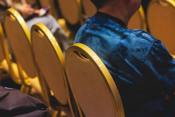Audience at the modern conference hall listens to panel discussion, people on a congress together listen to speaker on stage at convention, business seminar, amphitheater venue for presentation