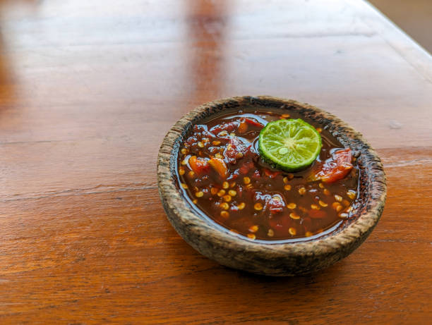 istock Red chili sauce (Traditional sambal Indonesia)  served on stone mortar with lime, on the wood table 2154214457