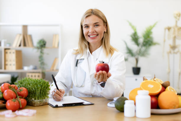 istock Portrait of female posing with apple while doing paperwork in doctor's office. 2154220253