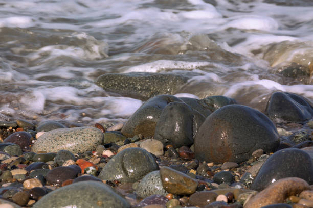 A wave runs over wet pebbles. The water's edge. Pebbles beach. Close-up