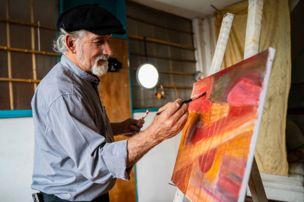 Man between 50-60 with gray hair and a large white beard, dressed in a French beret and comfortable and cool clothes, facing the camera in profile while making art and painting a beautiful painting in his studio, mixing paints, creating tones and giving brush strokes to finish your work
