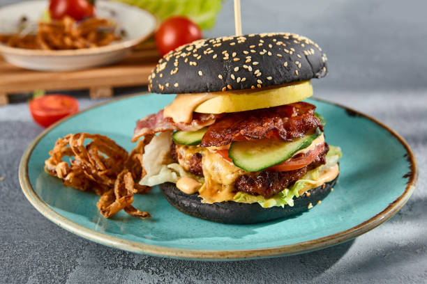 istock Gourmet black burger with bacon and crispy onions on a turquoise plate, gray textured backdrop with a hint of sunlight 2154236037