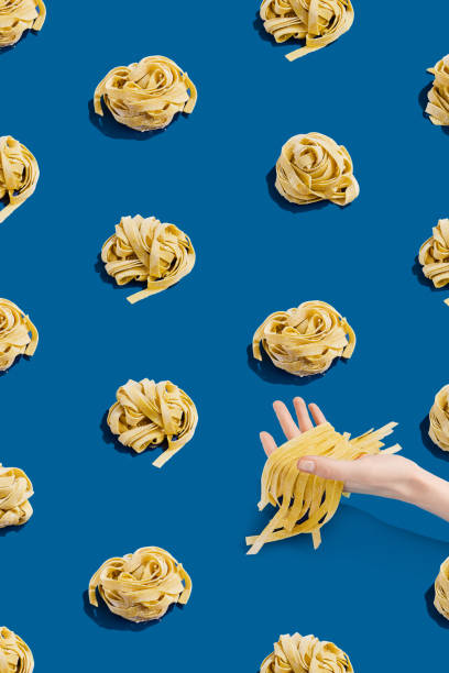istock Hand reaching for raw handmade pasta nests on blue background. Seamless pattern featuring fresh uncooked tagliatelle pasta arranged uniformly. Concept for Italian cuisine and culinary presentations 2154239993