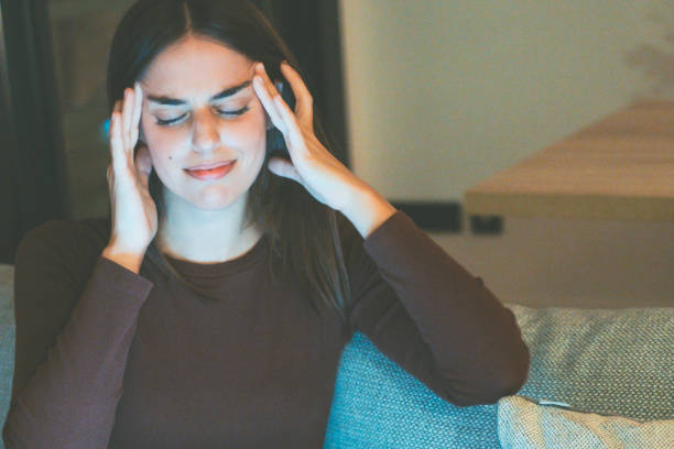 istock One woman massaging her heads for strong migraine headache sitting on the sofa after using laptop by night in online activity. People suffering from head pain and stress for failure. Head ache disease 2154243711
