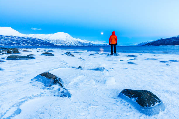 Man standing on the shore of a frozen ocean surrounded by snowy environment, Lyngen Alps, Norway, Scandinavia, Europe