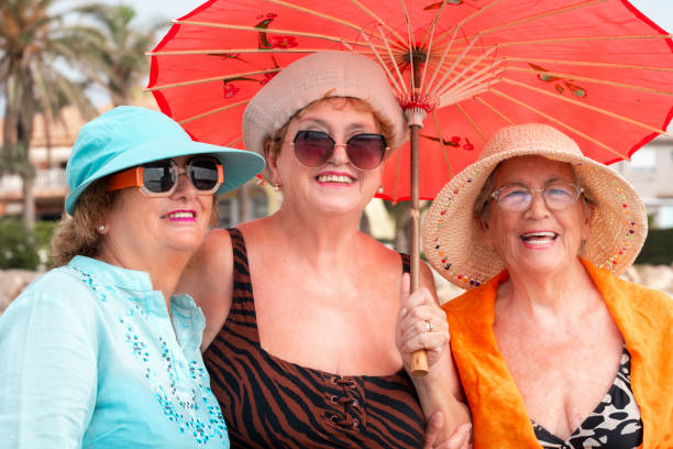 Group mature women wearing beach hats and smiling while standing on a tropical beach. Older ladies have fun in outdoor leisure activity in holiday vacation summer lifestyle. Elderly friends lifestyle