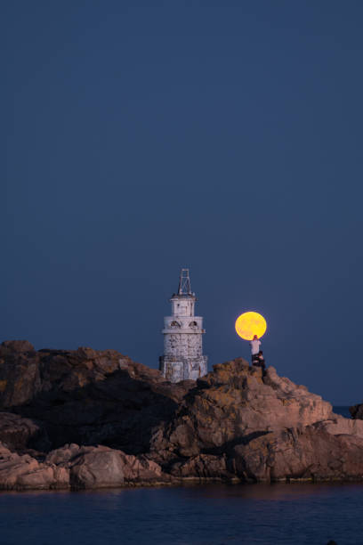 Full moonrise over lighthouse on the seashore. Supermoon rise. Full Sturgeon moonrise. August 1st 2023, Ahtopol, Burgas region, Bulgaria