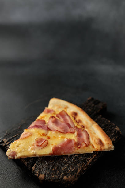 istock Piece of Pizza Carbonara on a black cutting board. Black background. Space for text 2154247827