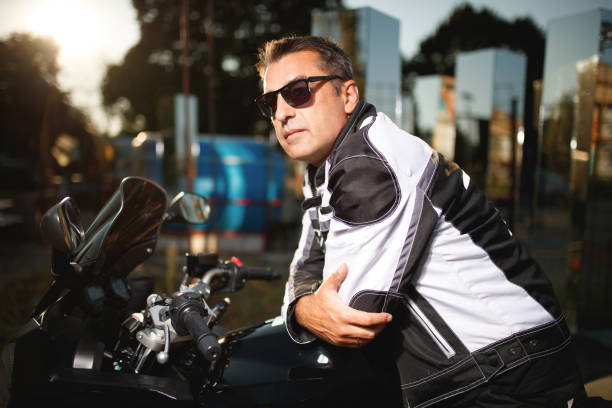 istock Mature man in biker jacket leaning on his motorcycle at sunrise 2154248199