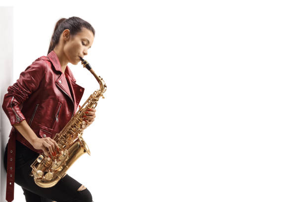 Young woman in a leather jacket playing a sax and leaning on a wall isolated on white background