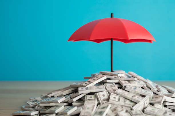 istock Heap US banknote is protected by red umbrella on wooden table blue wall background copy space. 2154250571