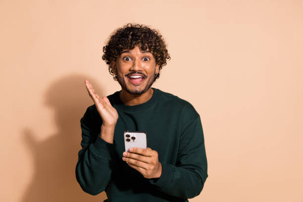 istock Photo of handsome impressed guy wear sweatshirt gettign sms modern gadget emtpy space isolated beige color background 2154254587