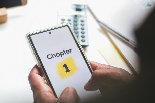 istock Man started reading an e-book on his phone. Chapter 1 displayed on the screen. Close-up, selective focus. 2154259335