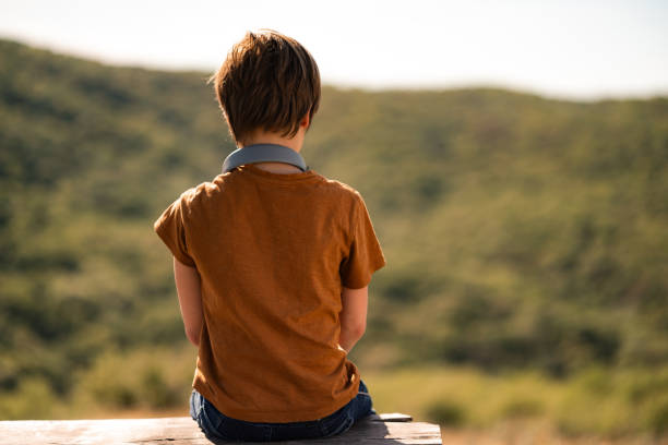 Rear view of a boy sitting alone on a bench in nature