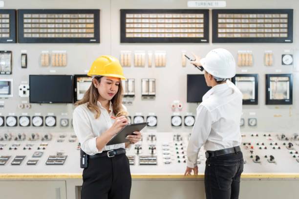 istock energy within the industrial landscape, two Asian engineers collaborate seamlessly at the power plant, utilizing laptops and blueprints to optimize operations and reduce environmental impact. 2154264221