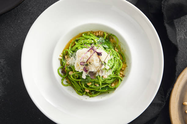 istock Elegantly plated pesto spaghetti with creamy stracciatella cheese and toasted pine nuts, served in a white bowl on a sleek black surface 2154265864
