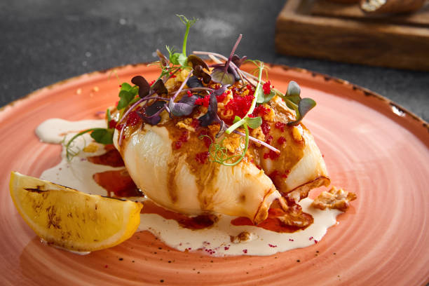 istock A succulent stuffed squid drizzled with creamy sauce, garnished with herbs, and served with grilled lemon on a peach-toned ceramic plate against a dark textured background 2154265892