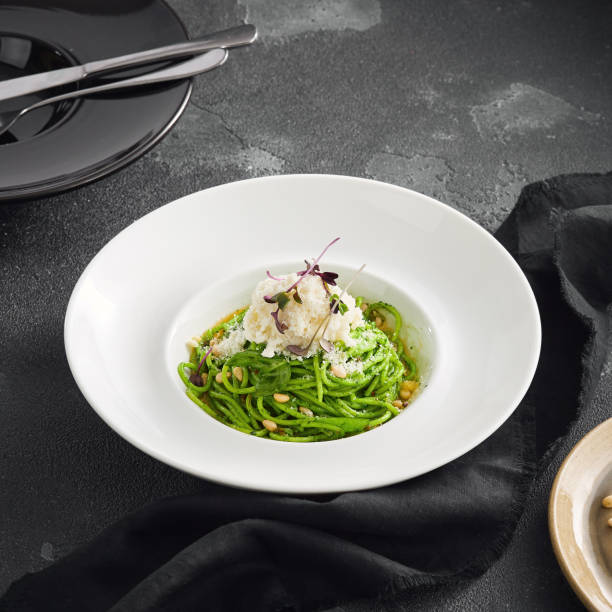 istock Elegantly plated pesto spaghetti with creamy stracciatella cheese and toasted pine nuts, served in a white bowl on a sleek black surface 2154265910