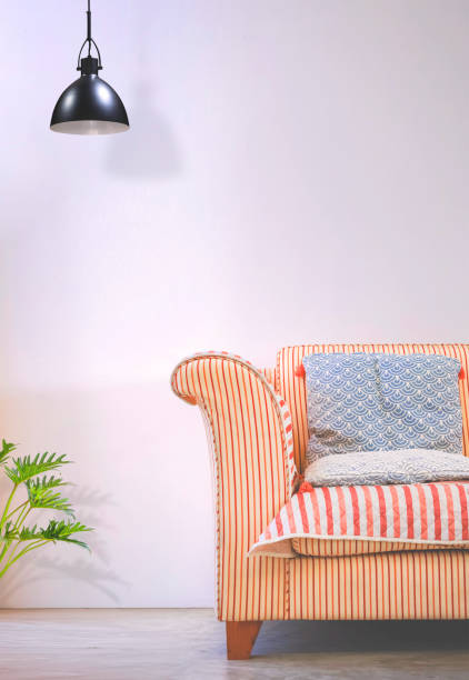 istock Comfortable fabric beige sofa and blue cushion with modern black aluminum ceiling lamp on white cement wall in vintage living room and vertical frame 2154266557