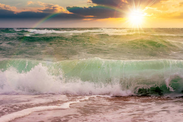 seascape with waves crashing the beach at sunset. beautiful summer scenery at the black sea with rainbow over horizon line in evening light