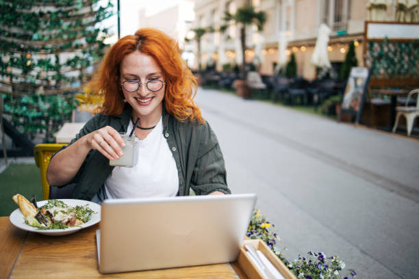istock A young red-haired woman is sitting in a cafe , eating a Caesar salad and using a laptop 2154275954