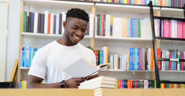 istock Cheerful student studying in library, holding book, sitting by bookshelf, smiling, focused on academic research. 2154280452