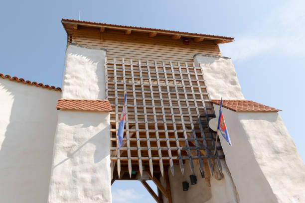 Close-up of a historic medieval fortress gate with flags, showcasing ancient architecture against a clear blue sky.