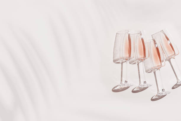 istock Long sparkling wine glasses top view with palm leaf shadow and light effects at sunlight, summer day festive drinks on white background, banner with copy space. Top view champagne rose wine 2154286255