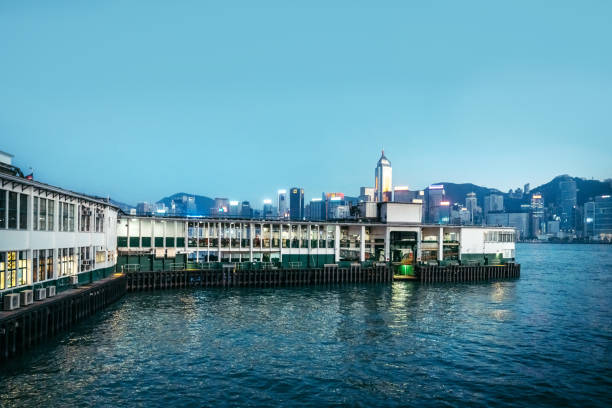 A scenic view of Hong Kong's skyline and waterfront pier during twilight, showcasing illuminated buildings and a serene water scene.