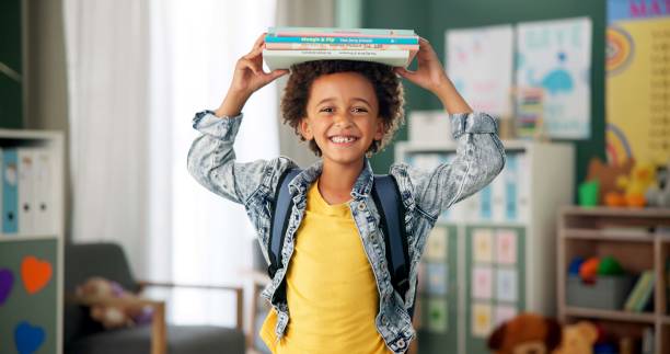 istock Child, face and book on head in school classroom for education learning in kindergarten, scholarship or happy. Kid, smile and knowledge academy for student creativity as reading, lesson or library 2154290470