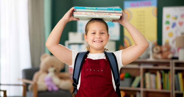 istock Face, girl and student with books on head, smile and education with knowledge, learning and confident. Portrait, school and kid with fun, playing and childhood development with happiness and cheerful 2154290494