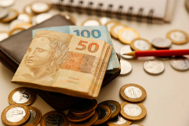 fifty reais notes and other notes and coins on the table with wallet, pencil and notebook
