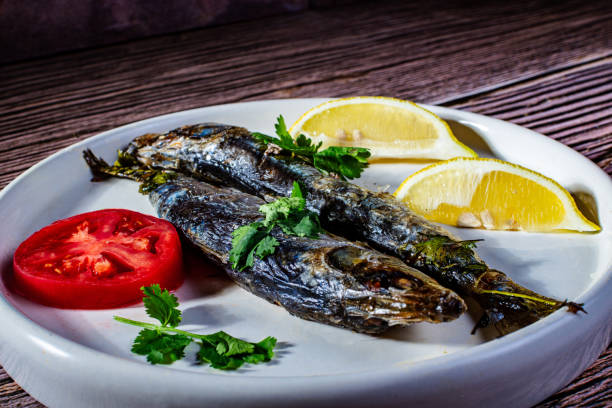 A plate of fish and tomatoes with a lemon wedge on the side