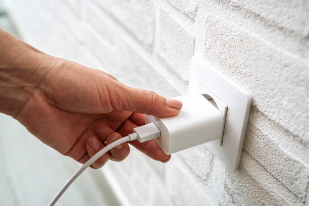 Close up of hand plugging/unplugging device charger in electrical wall socket