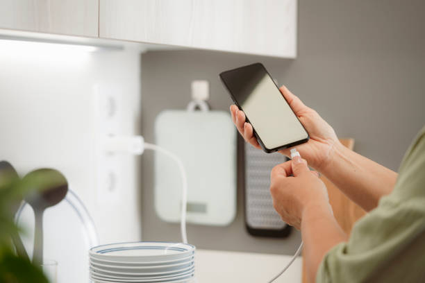 istock Woman in kitchen plugging mobile phone battery charger cable 2154325024
