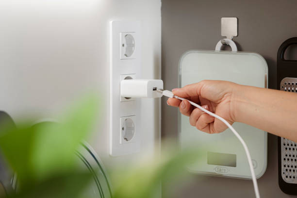 istock Woman in kitchen plugging USB cable to a wall electric charger 2154325039