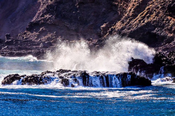 The ocean is crashing against a rocky shoreline, creating a powerful and dramatic scene. The waves are high and the water is choppy, giving the impression of a stormy sea. The rocks are jagged