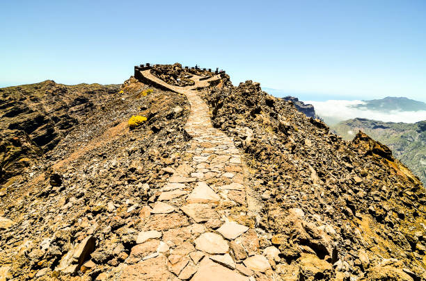 A rocky path leads to a mountain top. The path is made of stone and is surrounded by rocks. The sky is clear and the sun is shining brightly