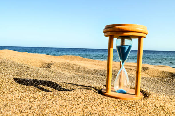 A wooden sand timer is sitting on the beach, with the sand around it. The sand timer is blue and white, and it is set to the number 1. The beach is calm and peaceful, with the ocean in the background
