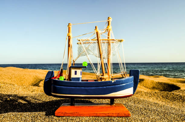 A small boat is sitting on the sand near the ocean. The boat is blue and white and has a small green ball on it. The scene is peaceful and serene, with the boat and the ocean as the main focus