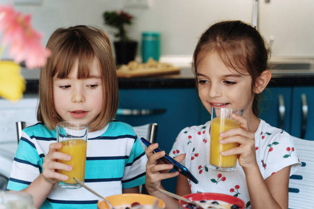 istock Kids sipping orange juice and using smartphone 2154342829