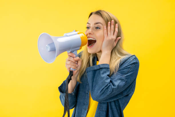 istock Smiling fun young woman in denim jacket posing isolated on yellow background in studi Scream in megaphone, announces discounts sale 2154344042
