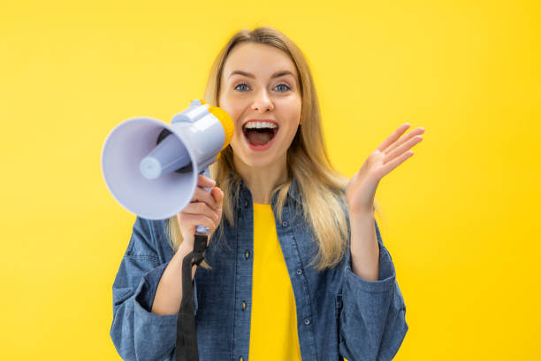 istock Smiling Young woman screaming in megaphone posing isolated on yellow background studio 2154344057